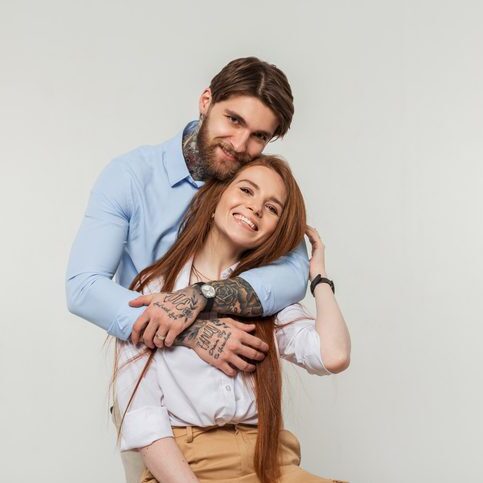 Happy fashionable beautiful couple in the studio. Stylish hipster handsome man with beard and tattoo hugging happiness redhead beautiful girl with smile on white background